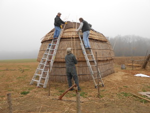 The first piece of synthetic bark is placed on the cap of the longhouse on a foggy, gray winter day!